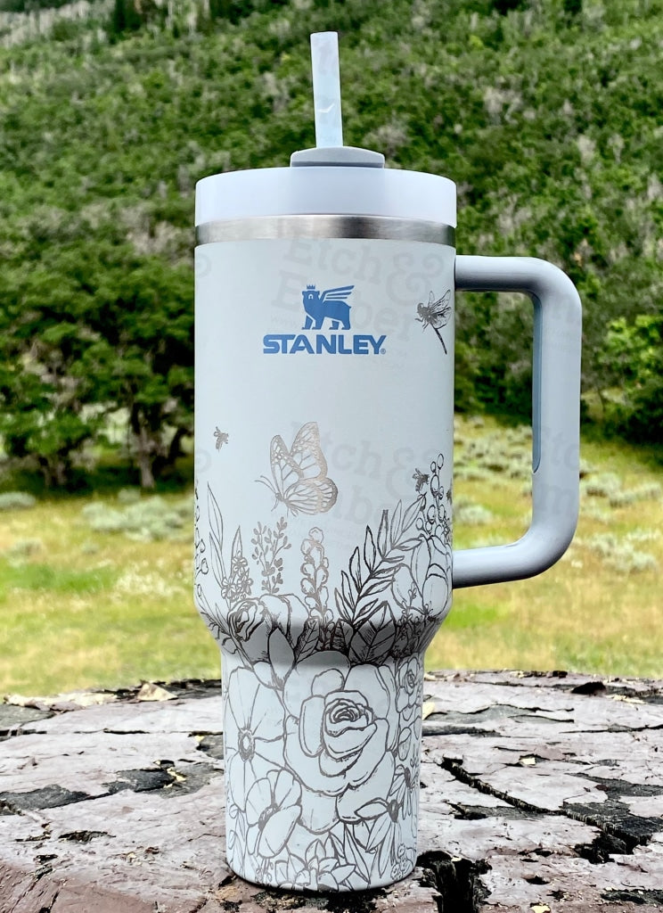 Stanley Adventure Quencher in a bright coral color, sitting next to a hiking backpack with the sturdy handle clearly visible