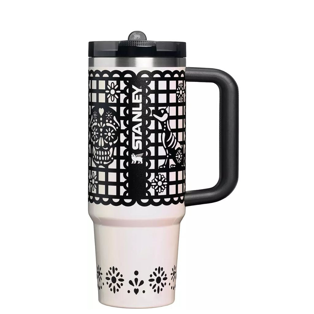 Stanley Salt Papel Picado tumbler featuring ivory-white finish, intricate black papel picado cut-paper-style borders, decorative sugar skull, stylized dog, floral motifs, black handle and lid, silver rim, and white Stanley logo.