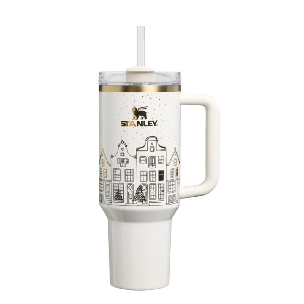 Stanley Salt Gingerbread tumbler with creamy ivory finish, black line-art European village houses, tiny evergreen trees, gold window accents, champagne-gold rim, metallic Stanley logo, matching ivory handle, and clear lid.