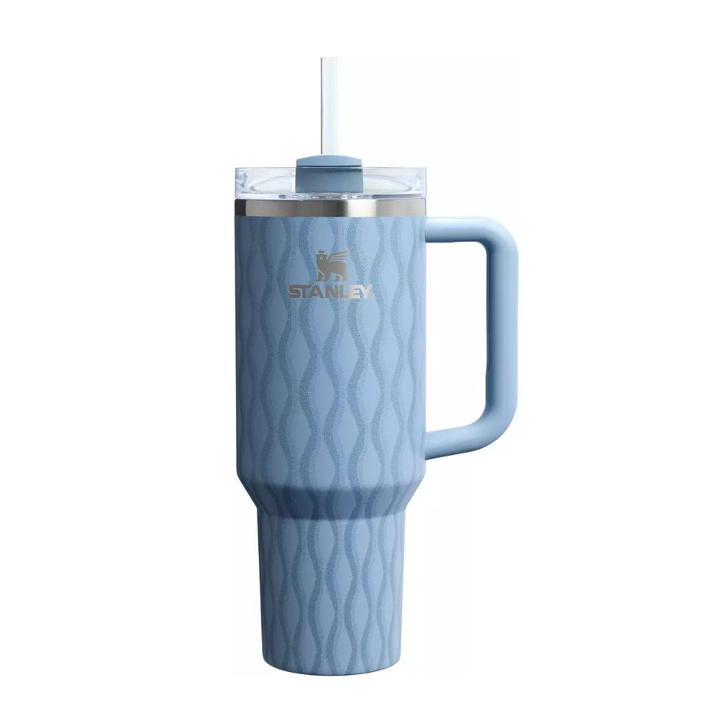 Stanley Slate Blue Drift tumbler featuring a muted dusty blue finish with a repeating wavy diamond pattern, matching light blue handle, clear lid, silver Stanley logo, and stainless steel rim.